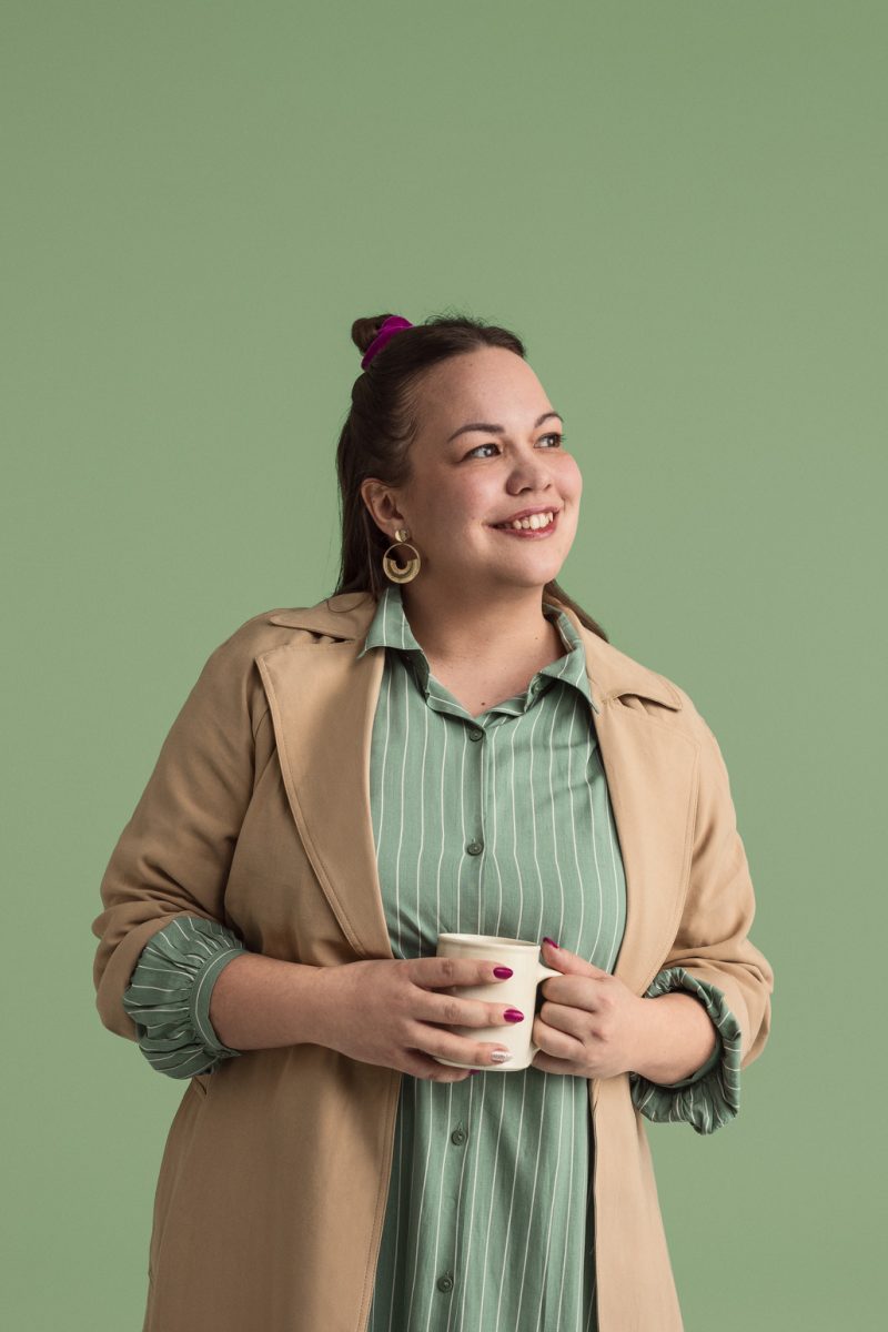 Nainen katselee hymyillen oikealle kahvikuppi kädessä.