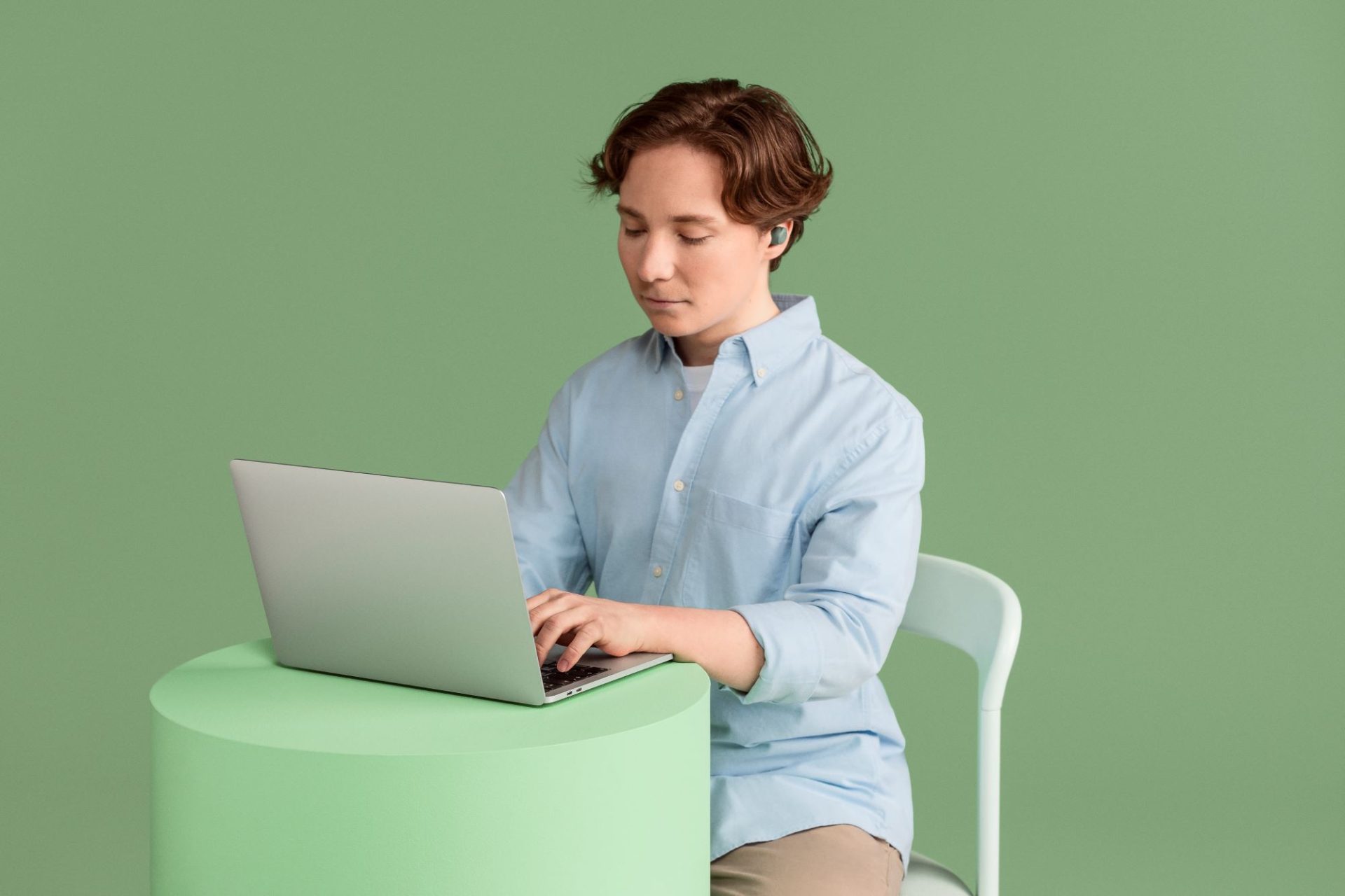 Nuori mies kirjoittaa tietokoneella langattomat kuulokkeet korvissaan.