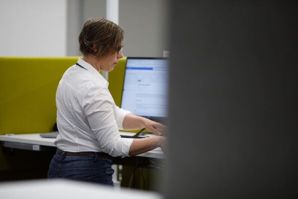 Valkopaitainen nainen työskentelee tietokoneen äärellä.