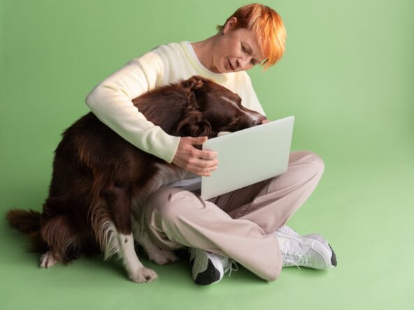 Nainen tutkii koira kainalossa tietokoneelta tulevia työttömyysturvan muutoksia